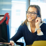 Picture of a female call centre agent wearing a headset sitting at a computer with red tinsel hanging on the back.
