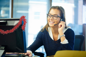 Picture of a female call centre agent wearing a headset sitting at a computer with red tinsel hanging on the back.